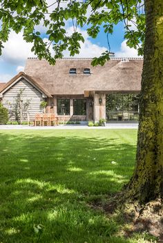 a large house sitting next to a tree on top of a lush green field under a blue sky