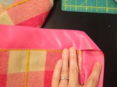 a person is sewing on a pink blanket with a ruler and measuring tape in the background