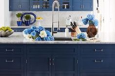 a kitchen with blue cabinets and flowers on the counter top in front of the sink