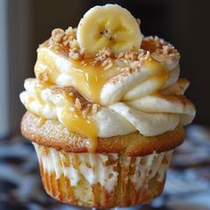 a cupcake topped with banana slices and cream frosting on top of a table