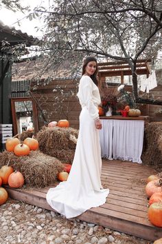 a woman in a white dress standing on a wooden deck surrounded by hay bales and pumpkins