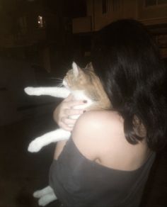 a woman holding a cat in her arms outside at night with the light from behind