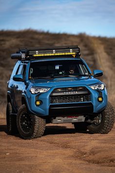 a blue four - doored vehicle driving down a dirt road