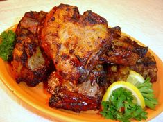 a plate with some meat on it and garnished with parsley next to lemon wedges