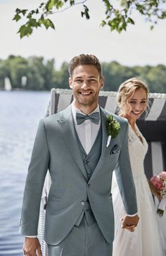 a bride and groom holding hands while standing next to each other on a dock near the water