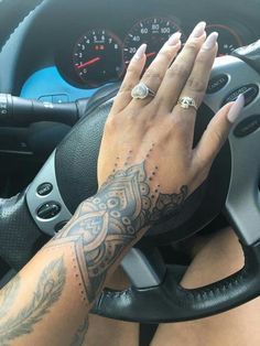 a woman with tattoos on her arm driving a car and holding the steering wheel in her hand