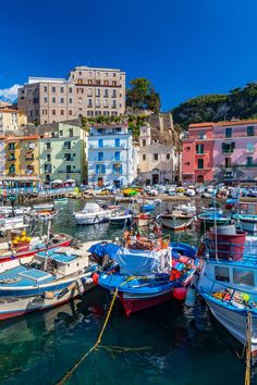 many small boats are docked in the water near some buildings and cliffs on a hill