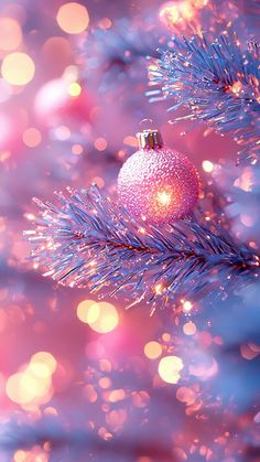 a pink ornament hanging from a christmas tree with blurry lights in the background