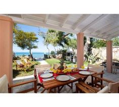 an outdoor dining area with table and chairs overlooking the ocean in front of a house