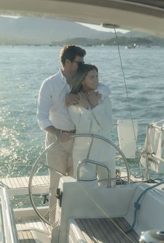 a man and woman standing on the deck of a sailboat looking at each other