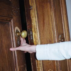 a person holding an object in their hand near two wooden doors with knobs on them