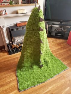 a crocheted green blanket on top of a wooden floor next to a fireplace