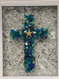 a cross made out of glass with blue and green beads on the bottom, in a white frame