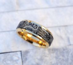 a gold and black wedding band with an intricate design on the inside is sitting on a marble surface