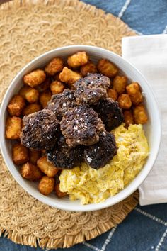 a bowl filled with meat and potatoes on top of a placemat next to a napkin