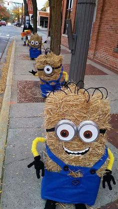 three hay sculptures are lined up on the sidewalk with googly eyes and one is wearing an apron