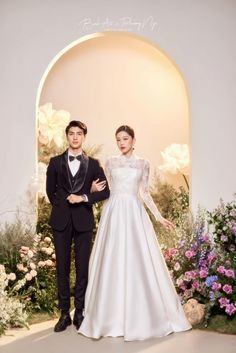 a man and woman standing next to each other in front of floral display with flowers