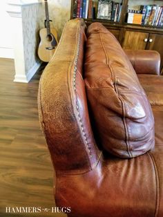 a brown leather couch sitting on top of a wooden floor next to a book shelf