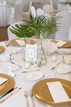 the table is set with gold and white plates, silverware, napkins, and a green plant