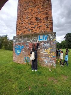 a woman standing next to a brick wall with graffiti on it and people walking by