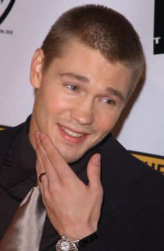 a man in a black shirt and tie with his hand on his chest smiling at the camera