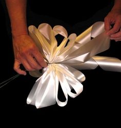 a person is making a paper flower out of white ribbon and silver ribbons with their hands