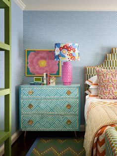 a bedroom with blue and green wallpaper, pink flower vase on dresser next to bed