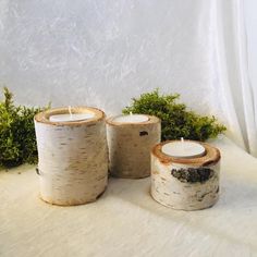 three white candles sitting next to each other on top of a table covered in snow