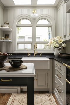 a white kitchen with black counter tops and gold trim on the windowsills is pictured in this image