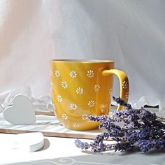 a yellow coffee cup sitting on top of a table next to lavenders and a white heart