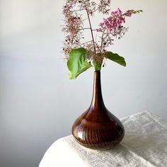 a brown vase filled with purple flowers on top of a white cloth covered tablecloth