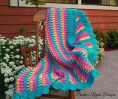 a crocheted blanket sitting on top of a wooden chair next to a flower garden