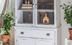 an old china cabinet with glass doors and drawers in the corner is decorated with potted plants