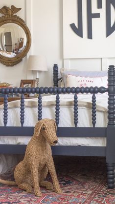 a dog sitting on the floor in front of a bed with blue posts and headboard