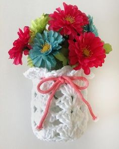 a crocheted vase with red and blue flowers in it on a white surface