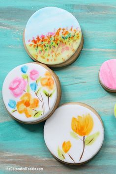 three decorated cookies sitting on top of a wooden table next to each other with flowers painted on them