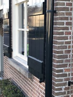 a brick building with black shutters and a cat sitting on the window sill