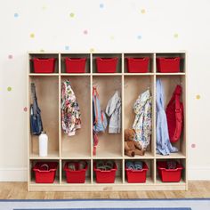 a child's coat rack with red baskets and clothes hanging on the wall next to a blue rug