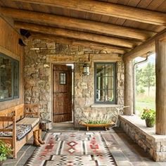 a porch with stone walls and flooring has a bench on the far side that leads to an outdoor sitting area