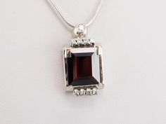 We transformed a Retro Era watch into this dazzling pendant! The garnet is exquisite, its deep scarlet hue brought to life with vibrant flashes of color from within. An array of diamond accents extends the sparkle to the entire pendant, creating a design that is truly glamorous.This pendant does not come with the chain shown. Please feel free to contact us, we will help you find the perfect chain for your style and budget!Metal: 14K White GoldGem: Pyrope Garnet totaling 6.00 CaratsGem Measurements: 13.5 x 11.6 mm, Emerald Cut Accents: 9 Diamonds totaling .36 Carats, SI1 in Clarity, H in ColorMeasurements: 27 x 14 mm, with bail Elegant Garnet Jewelry With Diamond Accents, Formal Garnet Jewelry With Gemstone Accents, Elegant White Gold Garnet Jewelry, Luxury Silver Garnet Jewelry, Luxury Polished Garnet Jewelry, Luxury Garnet Jewelry With Polished Finish, Elegant Garnet Jewelry With Gemstone Accents, Luxury Garnet Pendant Necklace, Pyrope Garnet