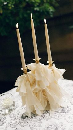 three candles are sitting on top of a table with ruffles and glassware