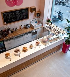 a counter with many desserts on it in front of a window and a motorcycle parked outside the window