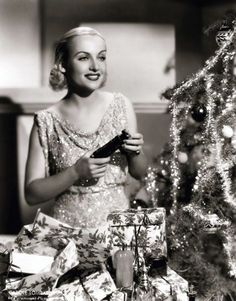 a black and white photo of a woman in front of a christmas tree with presents