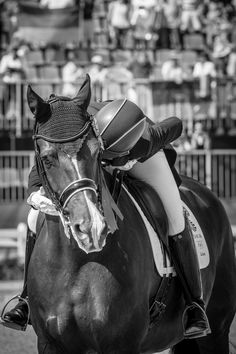 a woman riding on the back of a brown horse in front of an arena filled with people