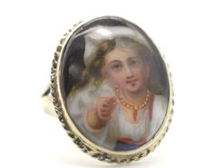 This ring is an exquisite specimen of Victorian-era craftsmanship, hailing from 19th-century France. It features a porcelain miniature, delicately hand-painted with a  portrait of a girl / young lady, a common romantic motif of the period. The ring's silver setting enhances the fine artistry of the portrait, indicative of the era's fascination with personal adornment.  Victorian jewelry often incorporated portraits, reflecting a culture rich in sentimentality and romanticism. Such a piece would Victorian Enamel Ring As Gift, Victorian Enamel Ring As A Gift, Victorian Enamel Ring For Gift, Victorian Oval Enamel Ring As Gift, Victorian Oval Enamel Ring As A Gift, Lady A, Victorian Jewelry, Portrait Girl, Antique Victorian