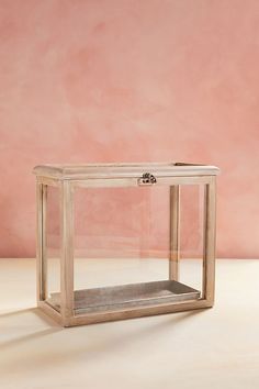 an empty glass box sitting on top of a white table next to a pink wall