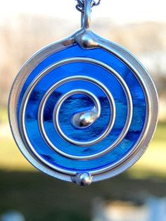 a blue glass pendant hanging from a chain on a window sill with grass in the background