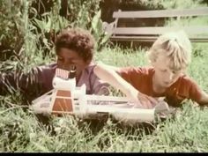 two young boys laying in the grass playing with a toy boat