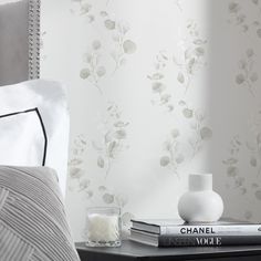 a nightstand with books and vases on top of it next to a wallpaper