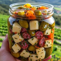 a hand holding a jar filled with pickles and cheese